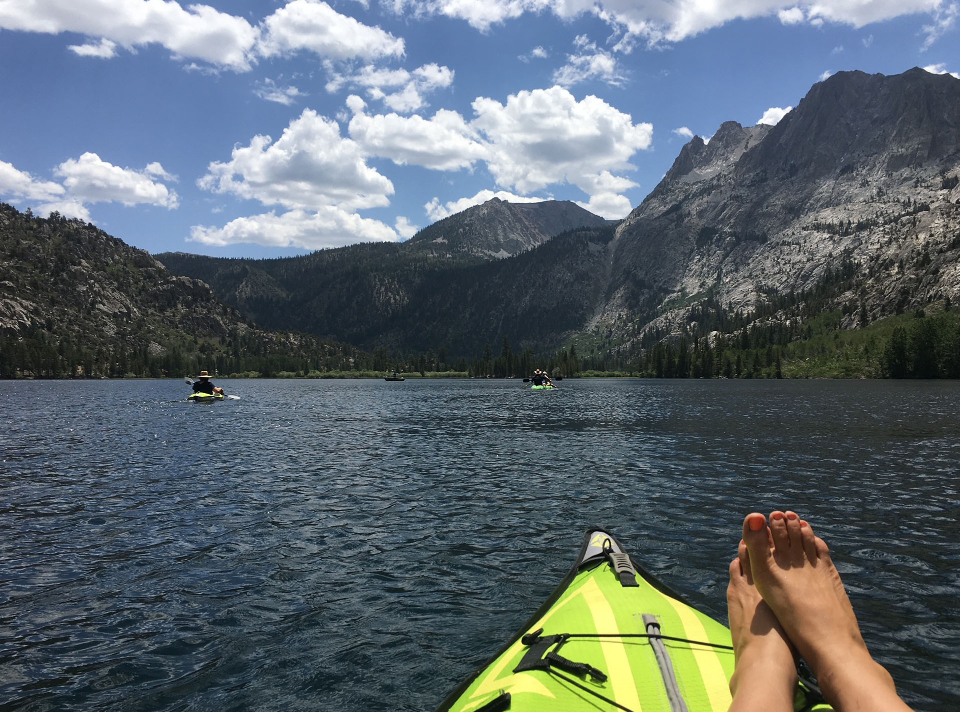 feet resting on green kayak floating in silver lake with view of california mountains and clouds in background