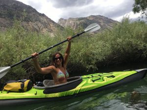 woman in a green kayak holding paddle over her head