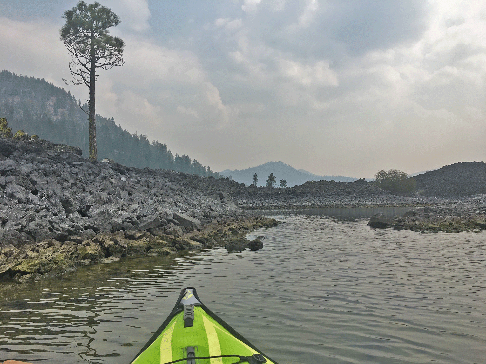 green kayak in butte lake in lassen volcanic national park, surrounded by volcanic rubbling with a few trees surrounding kayak