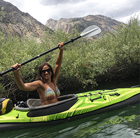 photo of shari kayaking rush creek on june lake loop in california. she is ina green kayak and is holder her paddle int he air above her head.