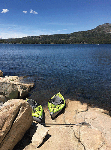 two bright green kayaks with paddles on granite slab at edge of deep blue lake