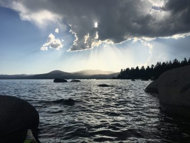 round rocks on lake tahoe at sunset near speedboat beach with dark cloud in sky