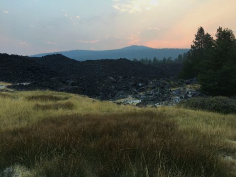 lassen volcanic national park at sunset. grass and brush in foreground, dark rocks in middle, mountain silouette and colored sky in background