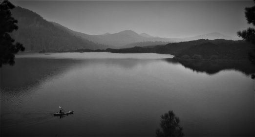 long kayaker in middle of butte lake surrounded by volcanic rubble with volcano in distance. black and white photo