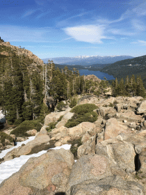 view overlooking donner lake with rocky foreground and snow capped mountains in background