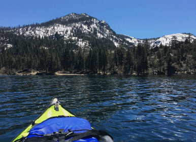 green kayak with blue life jacket on fallen leaf lake with snow covered mountain in background