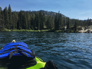 green kayak on gold lake with deepblue-green water and pine trees along coast in background