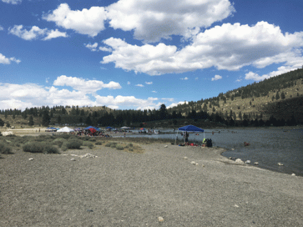 june lake beach with crowds of visitors and a few kayaks and sups in water on right side of photo