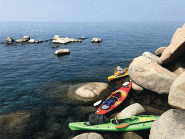 3 brightly colored kayaks on giant round boulders at the edge of lake tahoe california