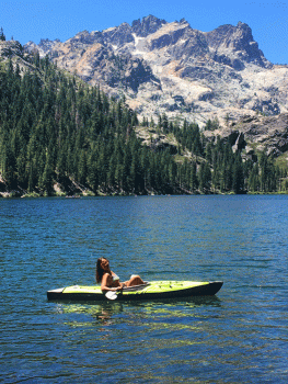 female kayaker in middle of sardine lake with rocky sierra buttes jutting above the lake in background